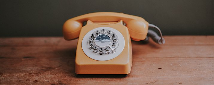 Ein oranges Telefon mit Wählscheibe auf einem Holztisch