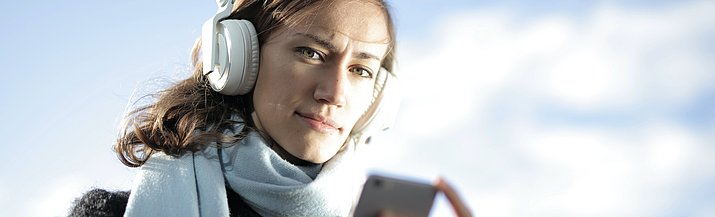 Frau mit Kopfhörern auf den Ohren und einem Smartphone on der Hand
