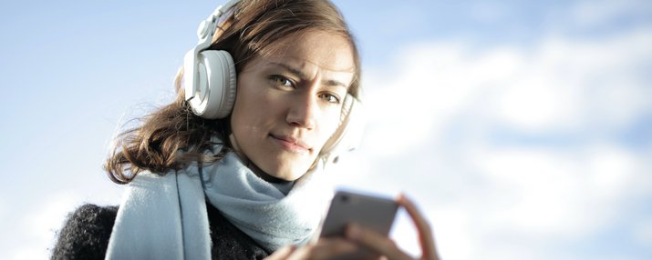 Frau mit Kopfhörern auf den Ohren und einem Smartphone on der Hand